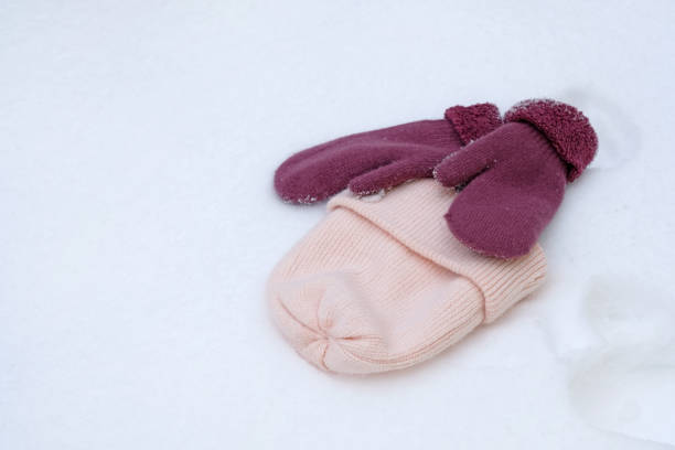 istock pink knitted hat and two mittens in the snow. 1213065083