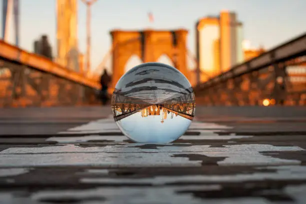The Brooklyn Bridge arch and surrounding buildings in focus through a lensball with the background blurred during sunset hour.