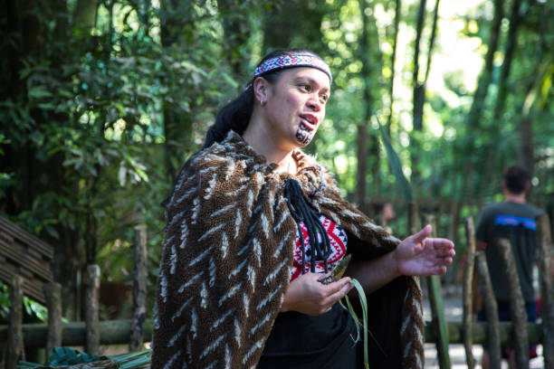 New Zealand: Maori Traditions A Maori woman demonstrates the tradition of weaving in front of a recreation of a typical Maori house from pre-European times. maori weaving stock pictures, royalty-free photos & images