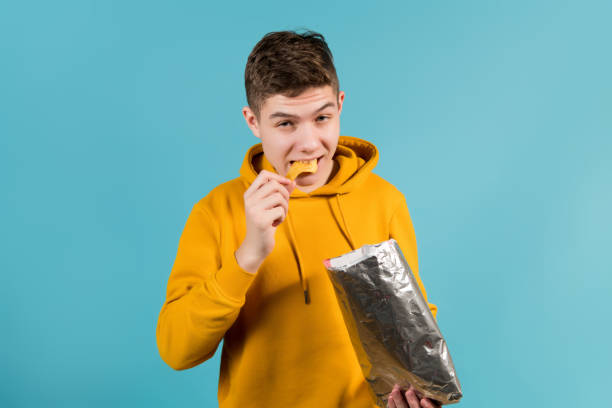 teenager in a yellow sweatshirt eats chips