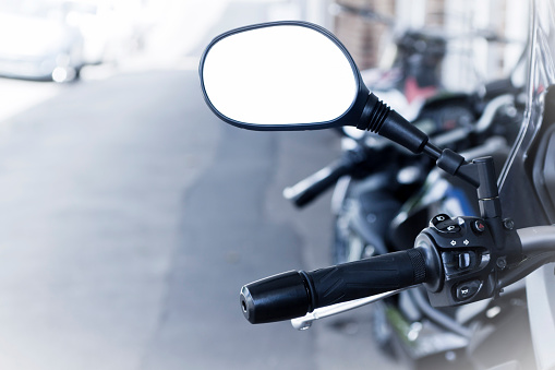 Closeup motorcycle handlebar with reversing empty mirror, full frame horizontal composition with copy space