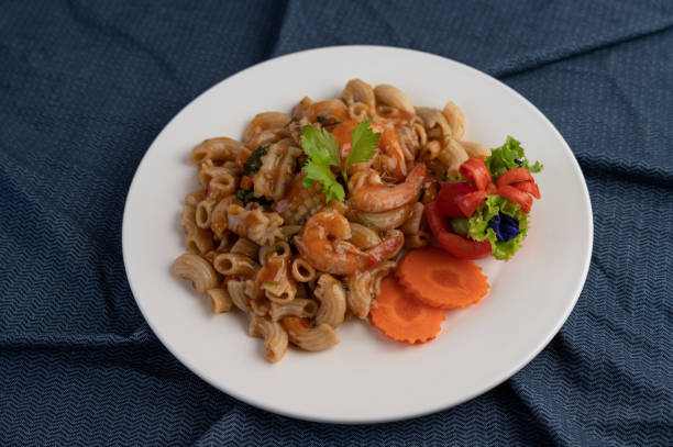 istock Stir shrimp macaroni on a white plate with carrots, tomatoes and salad. 1213100993