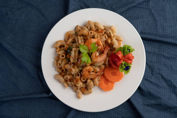 istock Stir shrimp macaroni on a white plate with carrots, tomatoes and salad. 1213101081