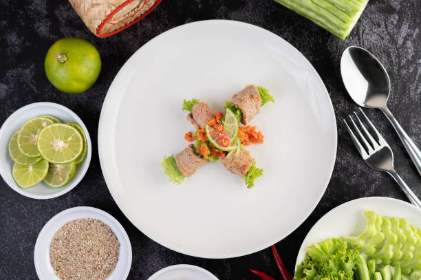 Spicy lime pork salad with bitter melon, galangal, chili, tomatoes and garlic in a white plate on a black cement floor.