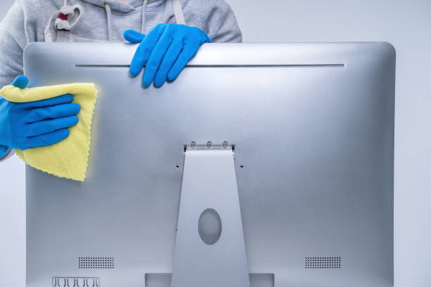 istock Young woman housekeeper in apron is doing cleaning silver computer screen with blue gloves, wet yellow rag. 1213118548