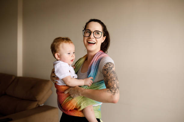 Young woman holding her baby and smiling Personal trainer working with a young mother and her baby baby carrier stock pictures, royalty-free photos & images
