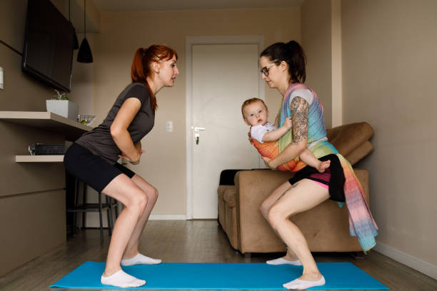 Young mother doing squats holding her baby with personal trainer Personal trainer working with a young mother and her baby baby squatting stock pictures, royalty-free photos & images