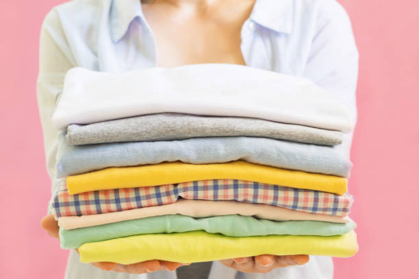 istock Modern Electric iron and stack of clothes on ironing board on pink background in laundry room. Household laundry ironing Woman holding Stacks of folded washed and dried clothes pile 1213125461