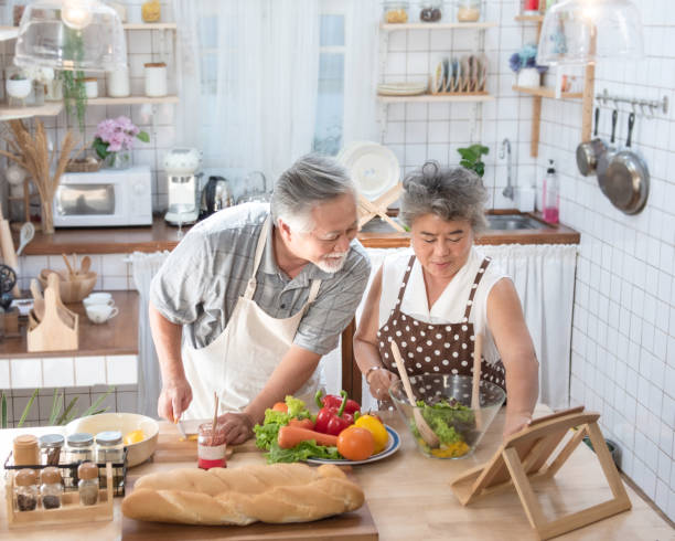 buscando nuevas recetas. pareja de ancianos de la tercera edad asiática usando tableta digital en la cocina, disfrutando de cocinar juntos en casa en el tiempo libre. - standing digital tablet couple love fotografías e imágenes de stock