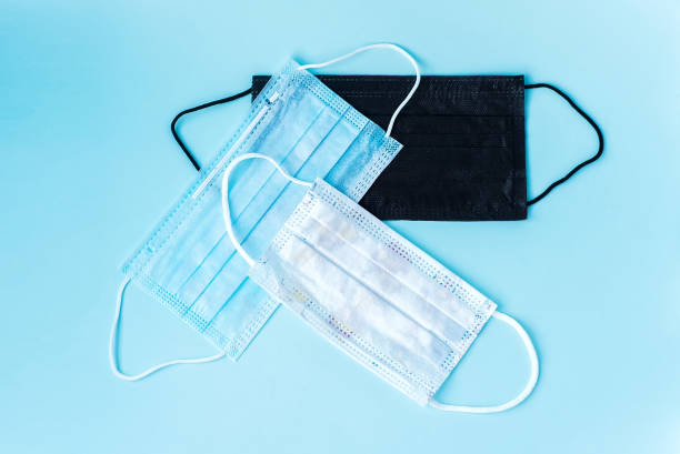 istock Black, blue and white PROTECTIVE masks for the whole family on a blue background. Typical three-layer surgical mask for covering the mouth and nose. The procedure with a bacterial mask. Protection con 1213132947