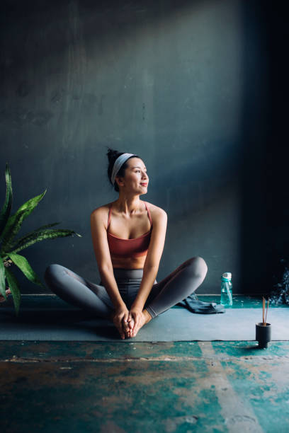 Asian Woman Sitting on an Exercise Mat and Warming Up for a Yoga Session Full-legth shot of a young Asian woman sitting on a yoga mat before exercising. exercise mat photos stock pictures, royalty-free photos & images