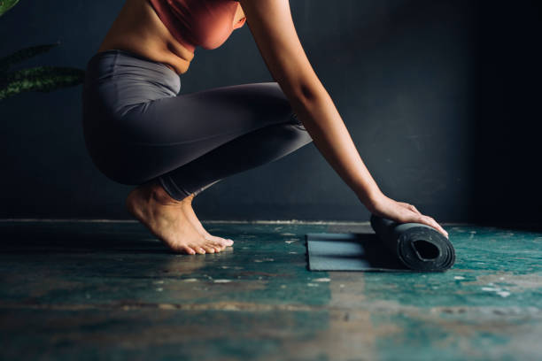 srotolare il tappetino: donna irriconoscibile che si prepara per la lezione di yoga - unrolling foto e immagini stock