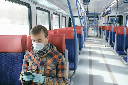 Disease outbreak, coronavirus covid-19 pandemic, virus protection, quarantine. Adult man with medical protective mask and gloves inside empty public transport using smartphone.