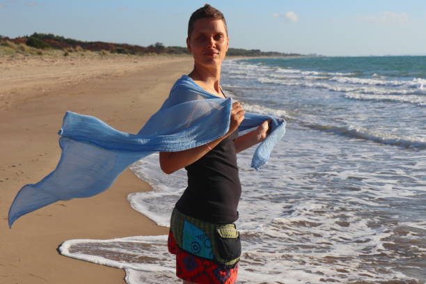 contented woman with mohawk haircut standing at the beach and looking into camera, holding a flying blue foulard - black blue escape multi colored imagens e fotografias de stock