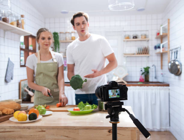 vídeo de gravação de câmera digital sem espelho profissional de casal caucasiano feliz cozinhando na sala de cozinha, câmera para fotógrafo ou vídeo e conceito de transmissão ao vivo, vlogger e blogueiro. - women home video camera camera vitality - fotografias e filmes do acervo