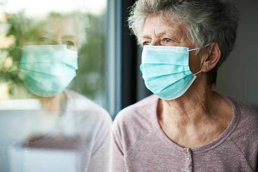 una anciana o abuela está usando un respirador o una máscara quirúrgica y mirando por la ventana photo