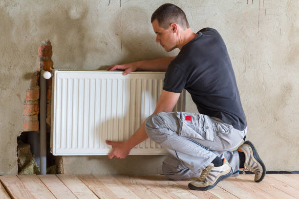 istock Young handsome professional plumber worker installing heating radiator in an empty room of a newly built apartment or house. Construction, maintenance and repair concept. 1213161886