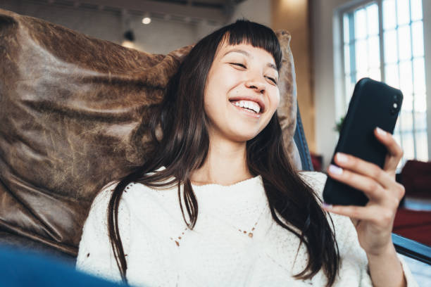 Portrait of smiling asian girl sitting in bright spacious with mobile phone in hands stock photo