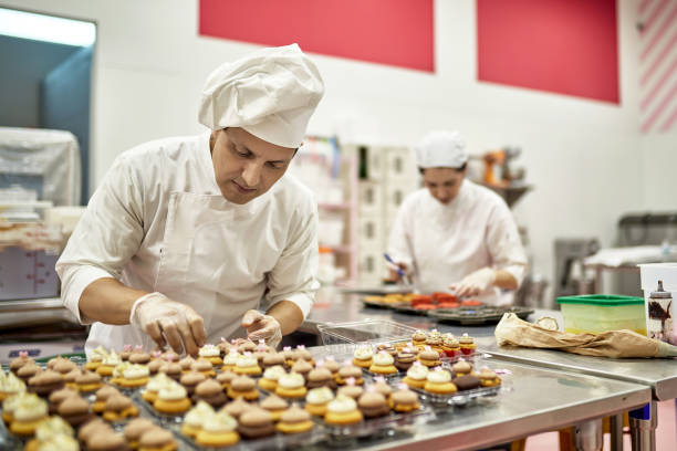 chef hispanoamericano decorando cupcakes veganos en cocina - commercial kitchen bakery front view baking fotografías e imágenes de stock