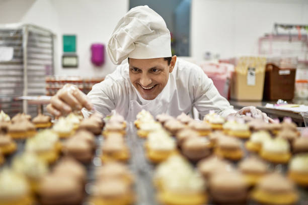 chef sonriente decorando cupcakes en cocina comercial - commercial kitchen bakery front view baking fotografías e imágenes de stock