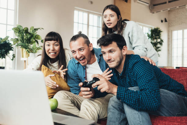 istock Group of four friends playing video games at home together using controller in big bright apartment 1213172053