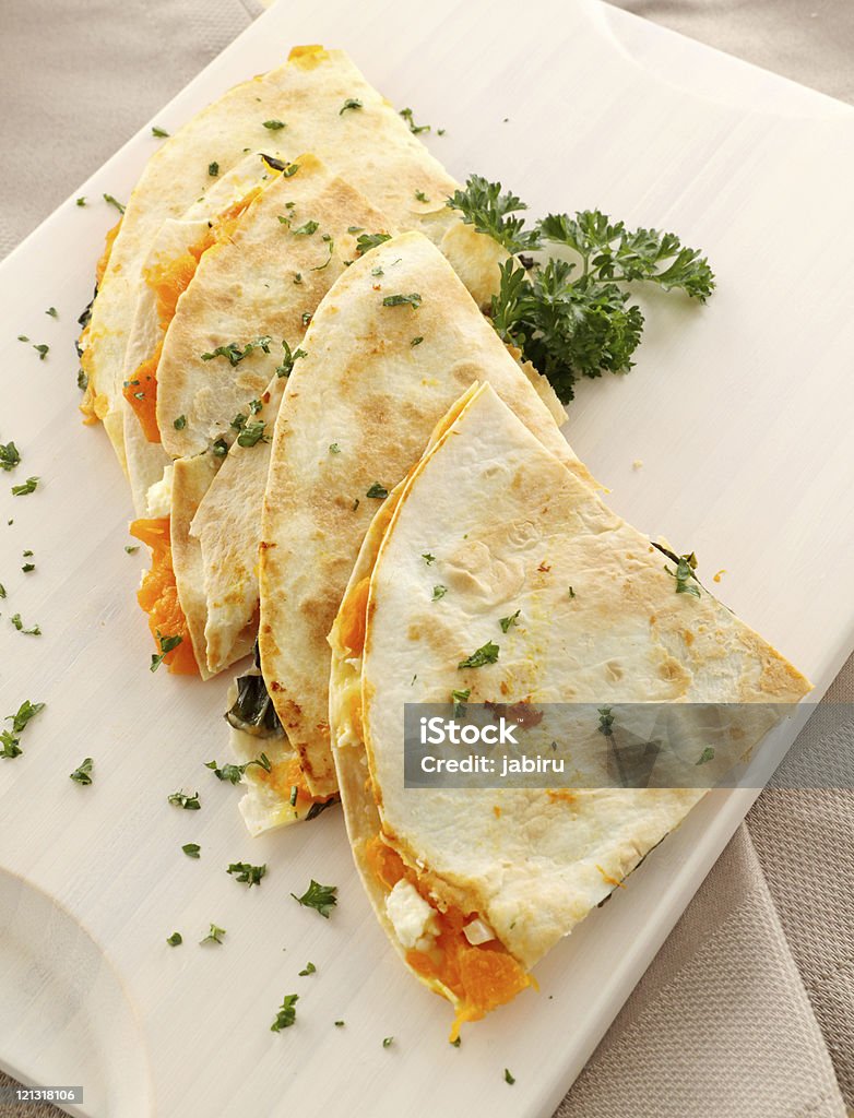 Toasted pumpkin quesadillas on white wooden board Delicious pumpkin quesadilla sliced and ready to serve with chopped parsley. Quesadilla Stock Photo