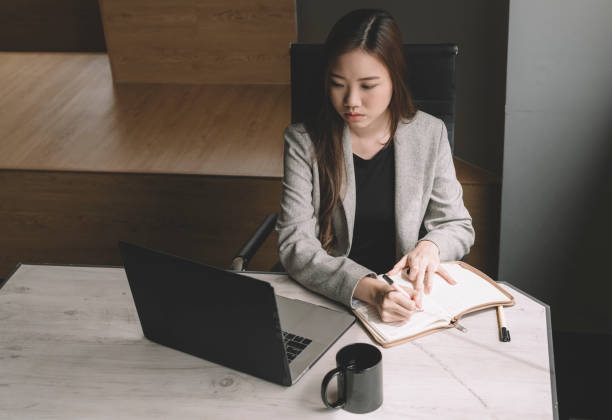 istock an asian chinese female young executive writing down note from her laptop in her work place 1213187097