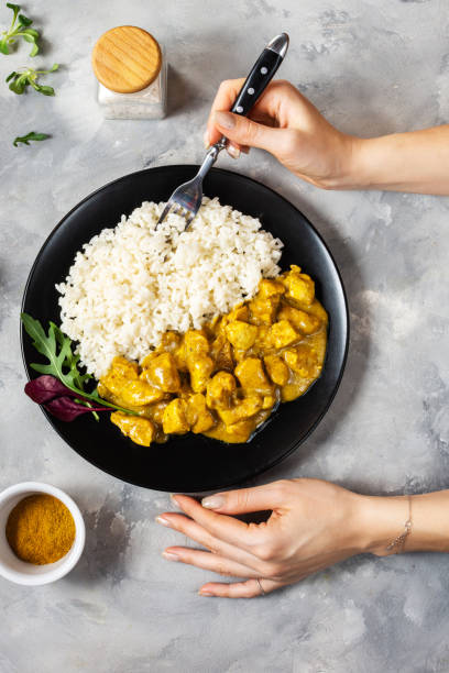 istock Female hand hold fork. Rice with chicken in curry sauce on a plate on concrete background 1213194306
