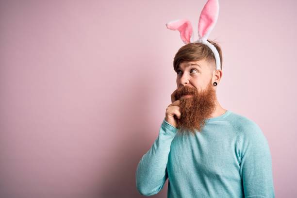 istock Hipster Irish man with beard wearing easter rabbit ears over isolated pink background with hand on chin thinking about question, pensive expression. Smiling with thoughtful face. Doubt concept. 1213199408