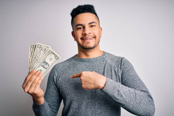 jovem homem bonito segurando um monte de notas de dólares sobre fundo branco isolado com rosto surpresa apontando o dedo para si mesmo - currency paper currency wealth human hand - fotografias e filmes do acervo