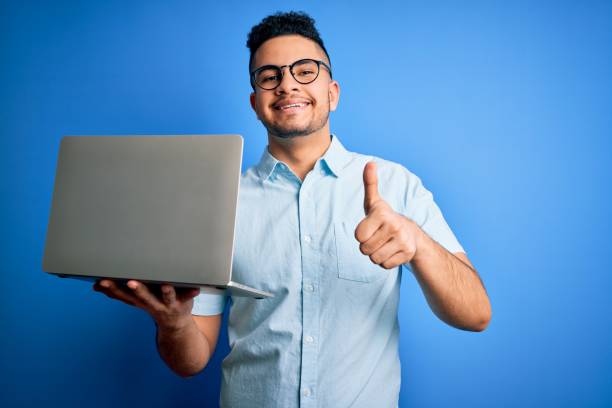 istock Young handsome businessman wearing glasses working using laptop over blue background happy with big smile doing ok sign, thumb up with fingers, excellent sign 1213201304