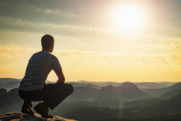 With reconciliation confident man sitting on the edge. Amazing view to born new day in hilly landscape far from people.