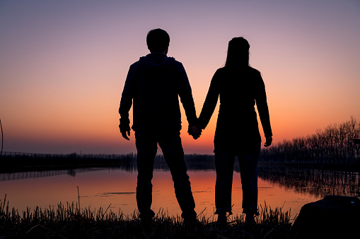 Silhouette of the couple are holding hands by the lake at sunset