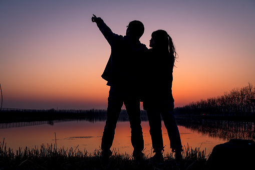 The couple are holding hands by the lake at sunset