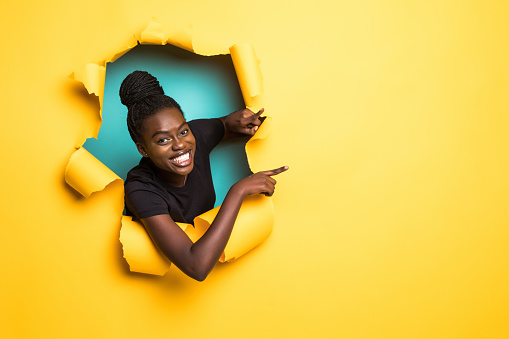 Young afro american woman pointed side and posing from yellow paper hole