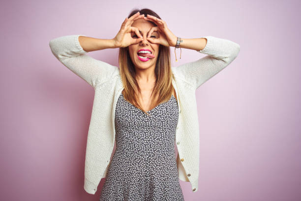 istock Young beautiful woman standing over pink isolated background doing ok gesture like binoculars sticking tongue out, eyes looking through fingers. Crazy expression. 1213211530