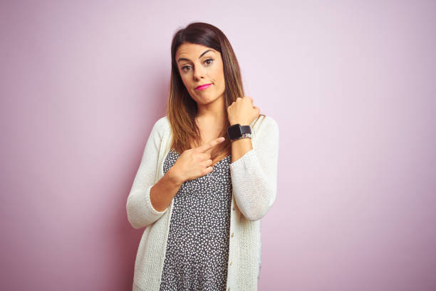 young beautiful woman standing over pink isolated background in hurry pointing to watch time, impatience, looking at the camera with relaxed expression - clock face clock deadline human hand imagens e fotografias de stock