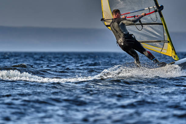 A male athlete is interested in windsurfing. He moves on a Sailboard on a large lake on an autumn day. A male athlete is interested in windsurfing. He moves on a Sailboard on a large lake on an autumn day. kiteboarding stock pictures, royalty-free photos & images