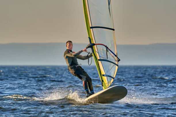 mężczyzna sportowiec jest zainteresowany windsurfingu. porusza się na sailboardzie na dużym jeziorze w jesienny dzień. - windsurfing zdjęcia i obrazy z banku zdjęć