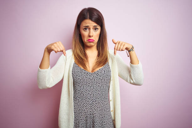 istock Young beautiful woman standing over pink isolated background Pointing down looking sad and upset, indicating direction with fingers, unhappy and depressed. 1213213665