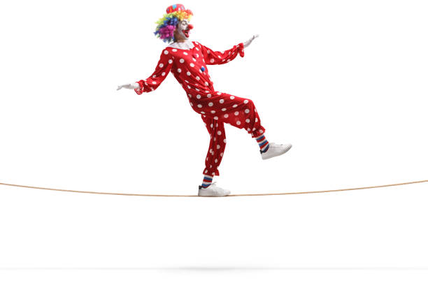 Full length profile shot of a clown walking on a rope isolated on white background