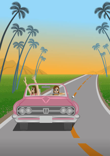 Two young women enjoying summer drive by the pink convertible in roadway at sunset