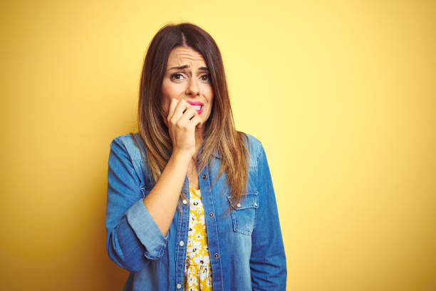 Young beautiful woman standing over yellow isolated background looking stressed and nervous with hands on mouth biting nails. Anxiety problem. Young beautiful woman standing over yellow isolated background looking stressed and nervous with hands on mouth biting nails. Anxiety problem. Phobia stock pictures, royalty-free photos & images
