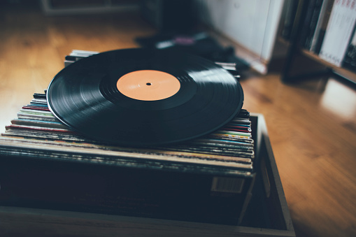 Caucasian female in nightwear holding a vintage vinyl record and drinking coffee at home in morning. Woman in pajamas looking at LP record and having morning coffee indoors.