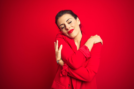 Young beautiful business woman standing over red isolated background Hugging oneself happy and positive, smiling confident. Self love and self care