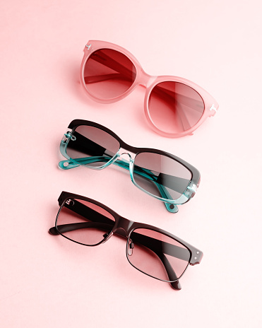 Collection of fashionable sunglasses on pink background. Sunglasses of different shapes and colors flat lay. Oval shaped sunglasses, oversized, wayfarer frames.