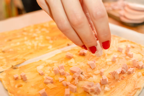 istock Close-up of a woman's hand preparing a pizza, sprinkling sausage on a rectangular pizza base 1213234135