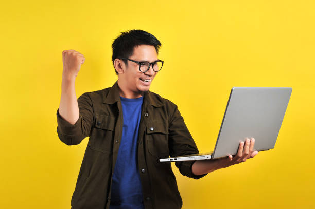 istock Asian man holding laptop with winning gesture, winning gift or lottery 1213234501