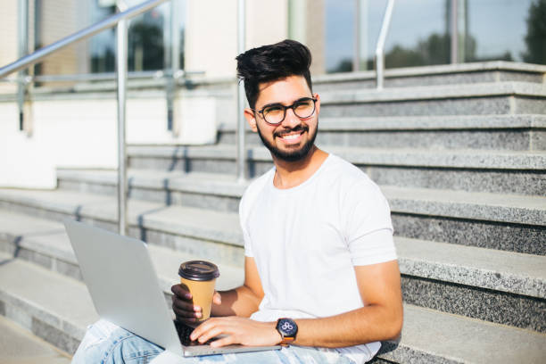 istock Handsome young indian man working on laptop while sitting outdoors on the stairs. 1213235786