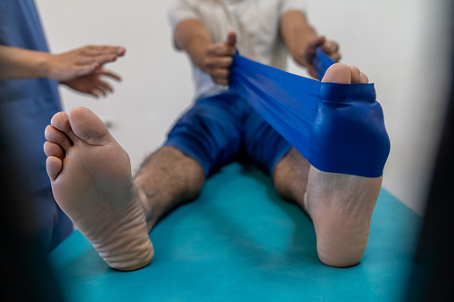 Close-up on a man stretching his foot with bands while doing physiotherapy at a clinic